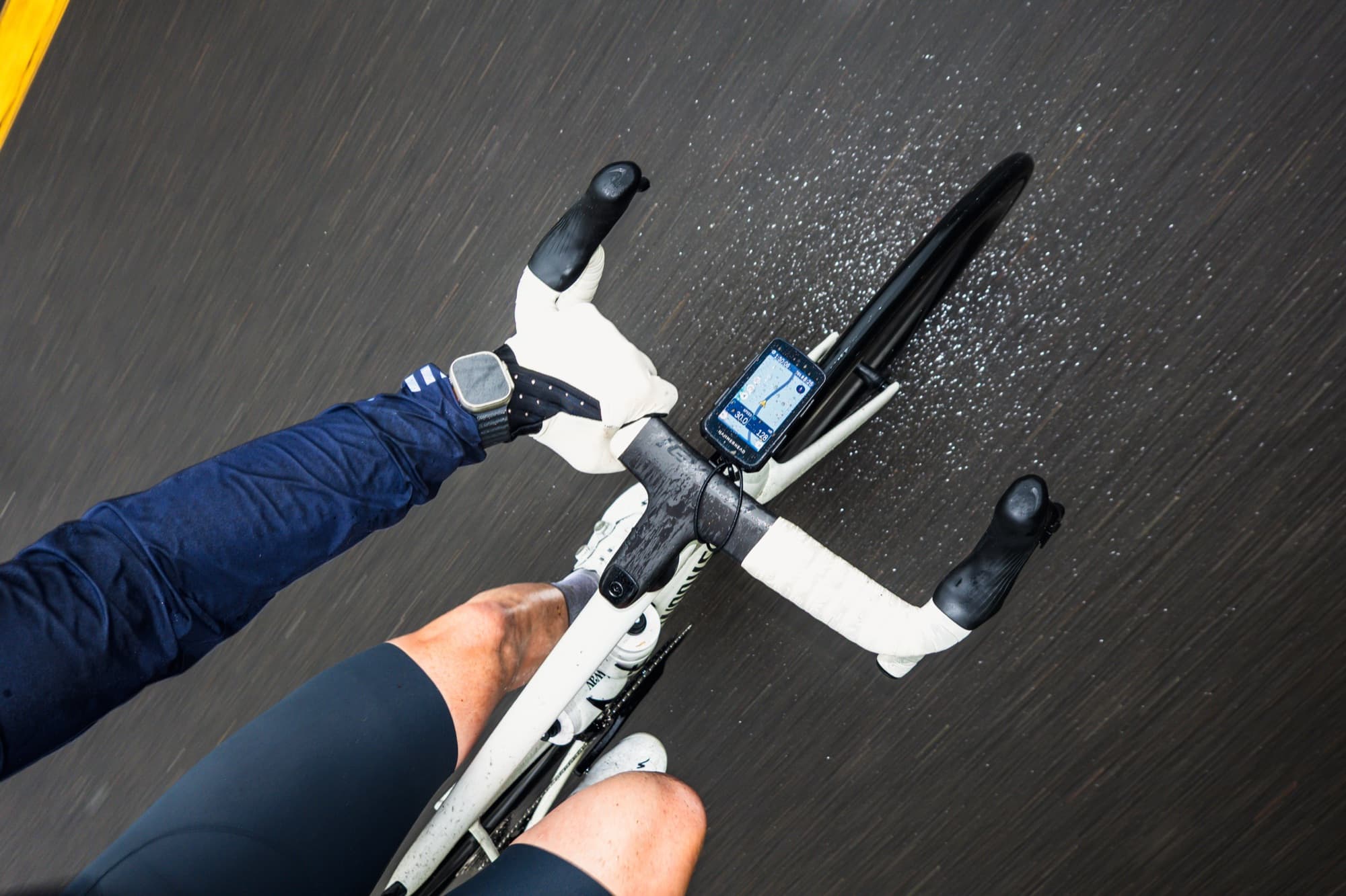 Looking down at handlebars and a bike computer on a wet road